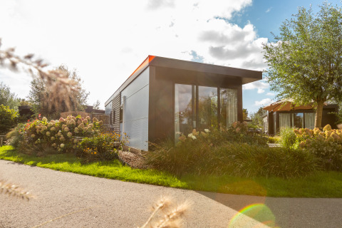 Chalet moderne Holiday chalet Comfort avec grandes fenêtres, entouré de fleurs et de jardins verdoyants.
