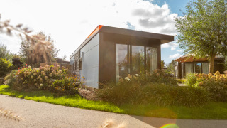 Chalet moderno Holiday chalet Comfort con grandi finestre, circondato da fiori e giardini verdi.