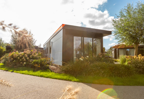 Chalet moderne Holiday chalet Comfort avec grandes fenêtres, entouré de fleurs et de jardins verdoyants.
