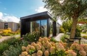 Modernes Ferienchalet Comfort im Ferienpark De Wiedense Meren, Niederlande, umgeben von Gartenblumen.