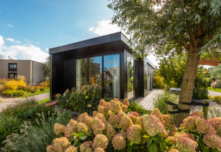 Modern holiday chalet Comfort at Holiday park De Wiedense Meren in the Netherlands, surrounded by lush plants.