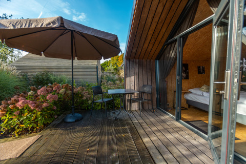 Terrazza in legno con tavolo, sedie e ombrellone al Tiny House nel Holiday park De Wiedense Meren, Paesi Bassi.