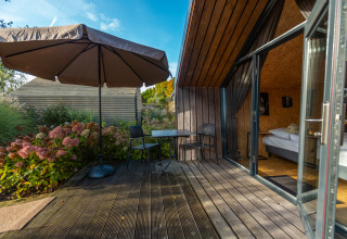 Terrazza in legno con tavolo, sedie e ombrellone al Tiny House nel Holiday park De Wiedense Meren, Paesi Bassi.