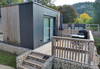 Moderne tiny house met houten terras en buitenzitje bij Kohnenhof in Luxemburg, omgeven door groen.