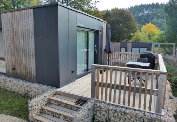Tiny house moderne avec terrasse en bois et coin salon extérieur au Kohnenhof au Luxembourg, entourée de verdure.