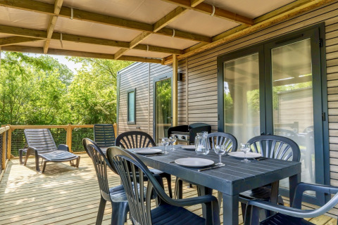 Outdoor covered terrace with dining set and loungers at COTTAGE Premium, Campsite Le Château, France.