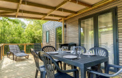 Outdoor covered terrace with dining set and loungers at COTTAGE Premium, Campsite Le Château, France.