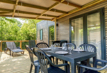 Udendørs terrasse med spisebord og liggestole ved COTTAGE Premium på Campsite Le Château i Frankrig.