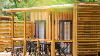 Hébergement glamping avec cabane en bois, terrasse, deux vélos et nature verdoyante en arrière-plan.