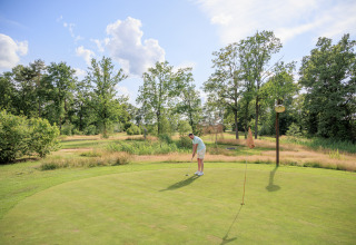 En mand spiller golf på grønsværen i Rekreationspark Kaps i Overijssel, Holland, omgivet af natur.