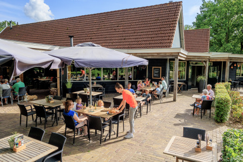 Area ristorante all'aperto al parco vacanze Kaps a Overijssel, Paesi Bassi, con ospiti e ombrelloni.