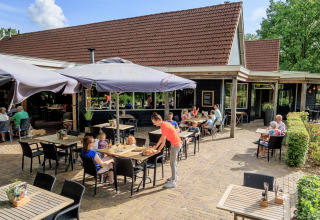 Terrasse d'un restaurant au parc de vacances Kaps à Overijssel, Pays-Bas, avec des convives et parasols.