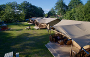 Tiendas glamping y mesas de picnic en el parque de vacaciones «Kaps» en Overijssel, Países Bajos, en un día soleado.