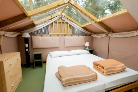 Dormitorio luminoso con tragaluz, cama doble y muebles de madera en Chianti Glamping Resort, Toscana, Italia.