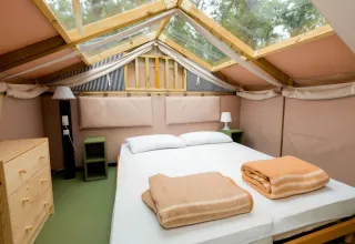 Bright bedroom with skylight, wooden furniture, and double bed at Chianti Glamping Resort, Tuscany, Italy.