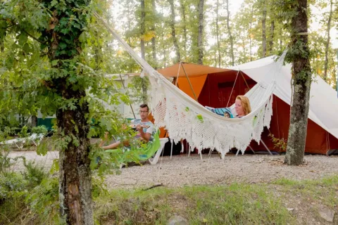 Pareja relajándose en Chianti Glamping Resort en la Toscana; una persona lee en hamaca, otra se sienta fuera de la tienda.