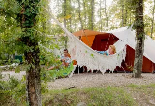 Koppel ontspant bij Chianti Glamping Resort in Toscane; één persoon leest in de hangmat, ander zit bij de tent.