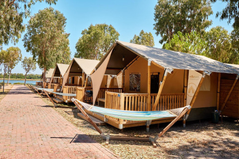 Tende safari presso Villatent Outback con amache e verande in legno, vicino a un lago e alberi.
