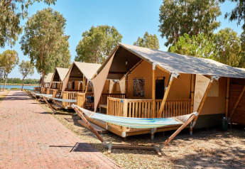 Tiendas safari en Villatent Outback con hamacas y terrazas, rodeadas de árboles cerca de un lago.