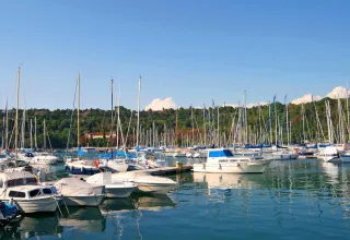 Barche e yacht ormeggiati nel porto turistico di Sistiana, Italia, circondati da colline verdi e cielo sereno.