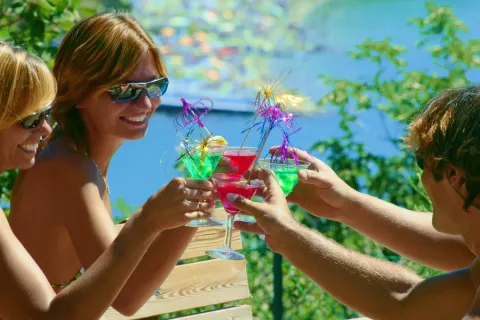 Tre amici con occhiali da sole brindano con cocktail colorati al Villaggio Mare Pineta, Friuli-Venezia Giulia, Italia.