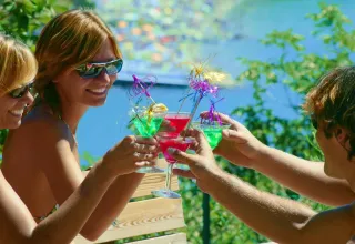Three friends in sunglasses toast with colorful cocktails outdoors at Village Mare Pineta holiday park, Italy.