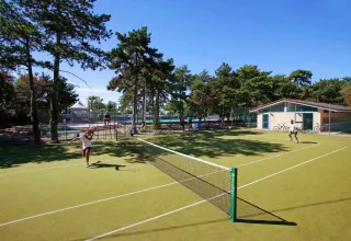 Outdoor tennis court surrounded by trees at Village Mare Pineta campsite in Friuli-Venezia Giulia, Italy.