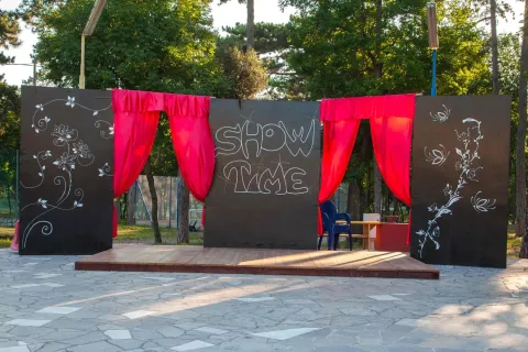 Palco all'aperto con tende rosse e decorazioni artistiche al Village Mare Pineta, Friuli-Venezia Giulia, Italia.