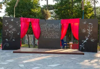Palco all'aperto con tende rosse e decorazioni artistiche al Village Mare Pineta, Friuli-Venezia Giulia, Italia.