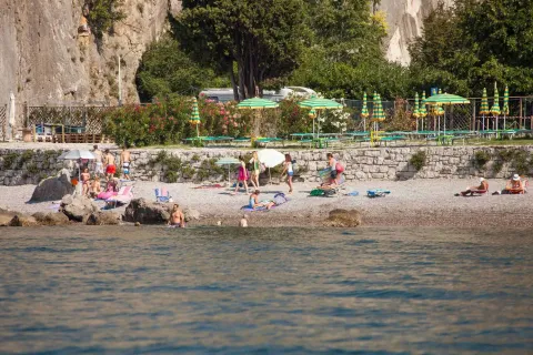 Persone si rilassano su una spiaggia di ciottoli vicino a Sistiana, Friuli-Venezia Giulia, Italia, tra ombrelloni verdi.