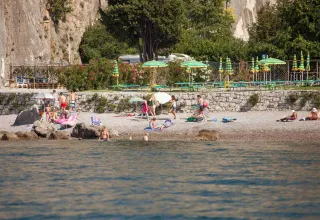 People relax on a pebble beach near Sistiana, Friuli-Venezia Giulia, Italy, surrounded by hills and umbrellas.