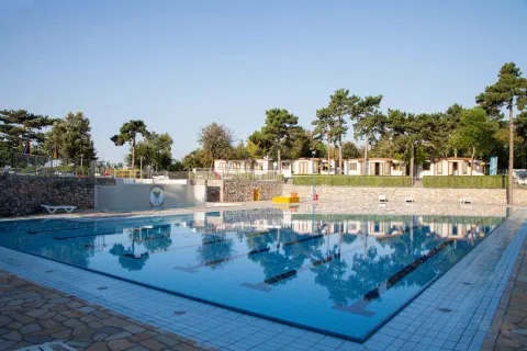 Piscina all’aperto al campeggio Village Mare Pineta, tra alberi e chalet in Friuli-Venezia Giulia, Italia.