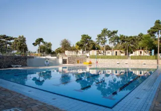 Schwimmbad auf dem Campingplatz Village Mare Pineta mit Ferienhäusern und Bäumen in Friuli-Venezia Giulia, Italien.