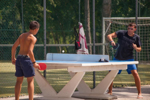 Due persone giocano a ping pong all'aperto su un tavolo di cemento al camping Village Mare Pineta, Italia.