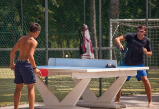Due persone giocano a ping pong all'aperto su un tavolo di cemento al camping Village Mare Pineta, Italia.