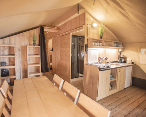 Interieur van een Safari Tent met houten meubels, keukenblok, eettafel en gezellige uitstraling.