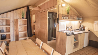 Indvendigt billede af et Safari Tent med træmøbler, tekøkken, spisebord og hylder, hyggelig atmosfære.