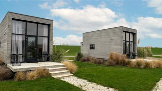Deux Tiny House 2+2 modernes avec grandes fenêtres et terrasse sur pelouse verdoyante sous ciel bleu.