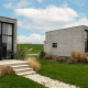 Two modern Tiny House 2+2 cabins with large windows, terrace, and greenery under a bright blue sky.