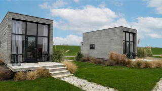 Twee moderne Tiny House 2+2 met grote ramen en terras, te midden van gras en onder een blauwe lucht.