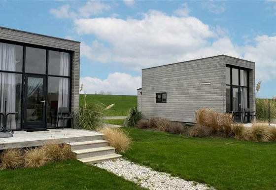 Twee moderne Tiny House 2+2 met grote ramen en terras, te midden van gras en onder een blauwe lucht.
