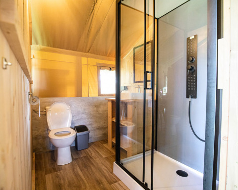Baño moderno en tienda safari con ducha, inodoro y decoración de madera en Hameau de l'Ourthe, Bélgica.