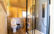 Moderne badeværelse i safaritelt med bruser, toilet og træinteriør på Hameau de l'Ourthe, Belgien.