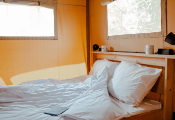 Gemütliches Bett mit weißen Kissen und Laken in einem Safarizelt im Hameau de l'Ourthe, Belgien.
