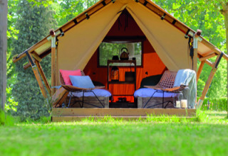 Tente safari avec sièges confortables, coussins et verdure, installée sous les arbres par beau temps.