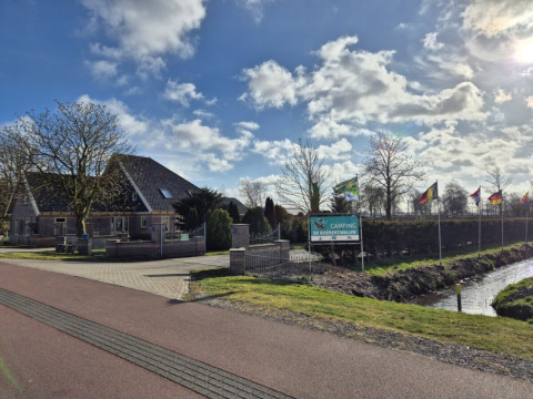 Photo of Safari tent at Campsite de Boerenzwaluw, Netherlands, with flag-lined driveway and house nearby.