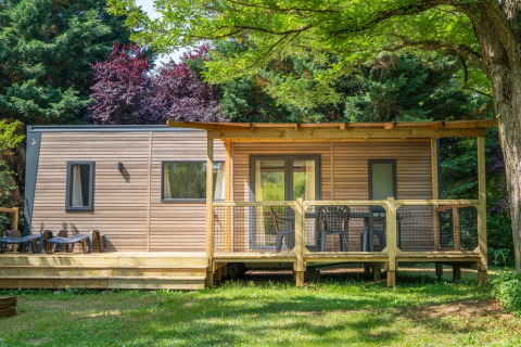 Outdoor view of COTTAGE Premium lodge with a wooden deck, garden furniture, and surrounded by trees.