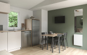 Cocina y comedor modernos en COTTAGE Premium del Camping Le Château, con pared verde y televisor.