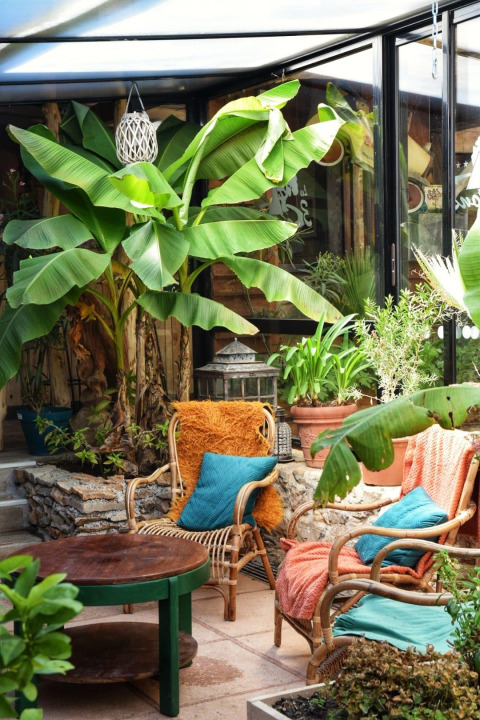 Sunny terrace with tropical plants, wicker chairs and colorful pillows at Les 3 Cantons campsite in Occitanie, France.