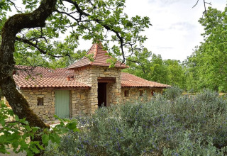 Stone house with a red tiled roof at Campsite Les 3 Cantons in Occitanie, France, surrounded by greenery.